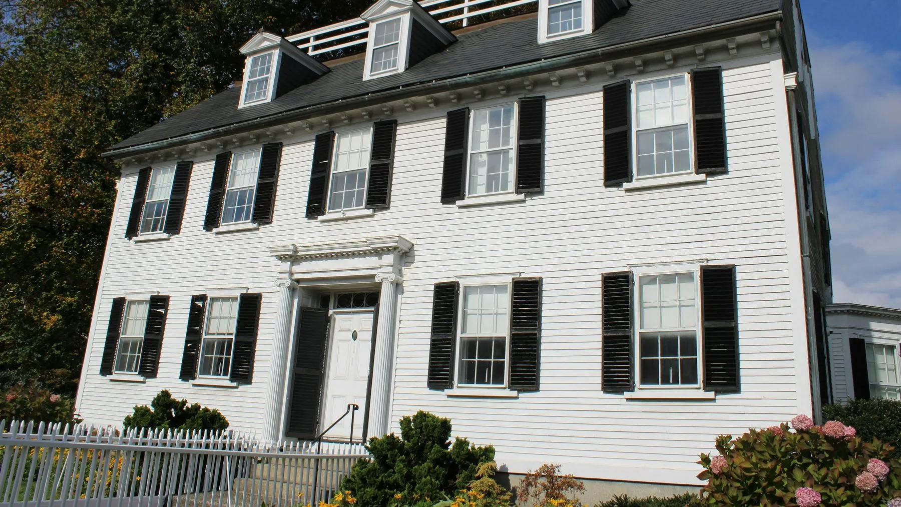 Classic white colonial house with black shutters and a picket fence on a New England street